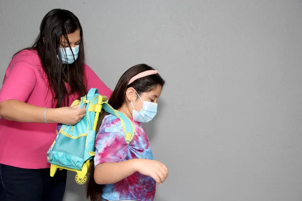 Latina mom and daughter prepare for back to school in the new normal due to the Covid-19 pandemic with backpack and face shield to protect from Coronavirus