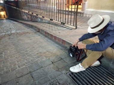 Şapkalı ve profesyonel kameralı bir erkek fotoğrafçı zemin kattaki bir tünele fotoğraf çekiyor.