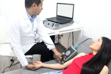 Koyu tenli Latin nörolog doktor kadın hastanın kolunda elektromiyografi ve somaduyusal canlandırma potansiyelleri üzerinde çalışıyor.