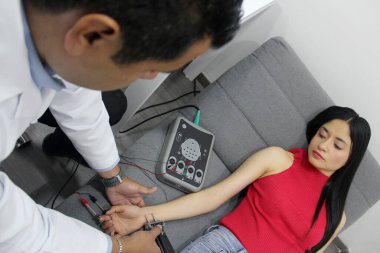 Koyu tenli Latin nörolog doktor kadın hastanın kolunda elektromiyografi ve somaduyusal canlandırma potansiyelleri üzerinde çalışıyor.