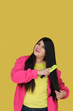 30 yaşındaki Latin kadın, uzun düz saçlarını tarıyor. Hasarlı, susuz ve karışık saçlardan muzdarip.