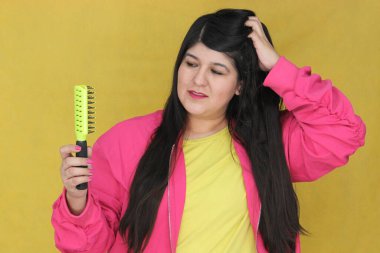 30 yaşındaki Latin kadın, uzun düz saçlarını tarıyor. Hasarlı, susuz ve karışık saçlardan muzdarip.