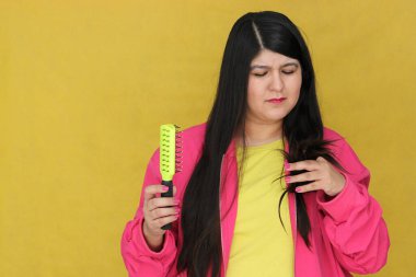 30 yaşındaki Latin kadın, uzun düz saçlarını tarıyor. Hasarlı, susuz ve karışık saçlardan muzdarip.