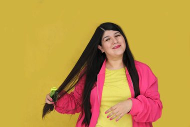 30 yaşındaki Latin kadın, uzun düz saçlarını tarıyor. Hasarlı, susuz ve karışık saçlardan muzdarip.