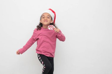 Kıvırcık kahverengi saçlı, Noel Baba şapkası takan 4 yaşındaki Latin kız Noel ve yeni yılı kutlamak için bastonla şarkı söylüyor.