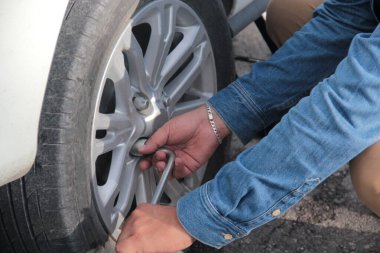 Yetişkin Latin bir adam lastik lastiğini ingiliz anahtarıyla değiştiriyor ve yedek lastiği takmak için fındıkları çıkarıyor.