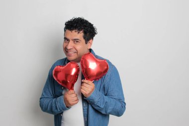 40 yaşındaki siyah saçlı ve kıvırcık saçlı Latin bir adam Sevgililer Günü 'nü kutluyor ve aşkını kalp şeklinde bir balon, gözlük, hediye ve oyuncak ayıyla gösteriyor.