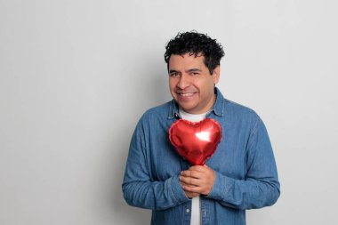 40 yaşındaki siyah saçlı ve kıvırcık saçlı Latin bir adam Sevgililer Günü 'nü kutluyor ve aşkını kalp şeklinde bir balon, gözlük, hediye ve oyuncak ayıyla gösteriyor.