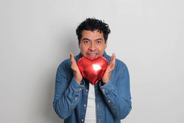 40 yaşındaki siyah saçlı ve kıvırcık saçlı Latin bir adam Sevgililer Günü 'nü kutluyor ve aşkını kalp şeklinde bir balon, gözlük, hediye ve oyuncak ayıyla gösteriyor.