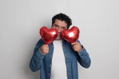 40 yaşındaki siyah saçlı ve kıvırcık saçlı Latin bir adam Sevgililer Günü 'nü kutluyor ve aşkını kalp şeklinde bir balon, gözlük, hediye ve oyuncak ayıyla gösteriyor.