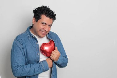 40 yaşındaki siyah saçlı ve kıvırcık saçlı Latin bir adam Sevgililer Günü 'nü kutluyor ve aşkını kalp şeklinde bir balon, gözlük, hediye ve oyuncak ayıyla gösteriyor.