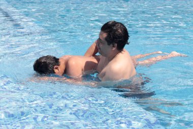 Bekar baba, 11 yaşındaki Latin oğluna havuzda yüzmeyi öğretiyor.