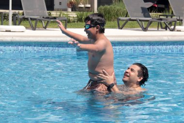 Bekar baba, 11 yaşındaki Latin oğluna havuzda yüzmeyi öğretiyor.