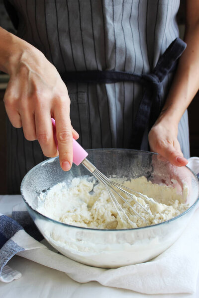 Домашнее хозяйство. Руки домохозяйки месят тесто в большой миске венчиком. Семейный праздник. Закрыть.