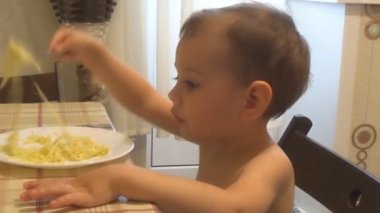 Küçük bir çocuk mutfakta çatalla masada makarna yiyor.