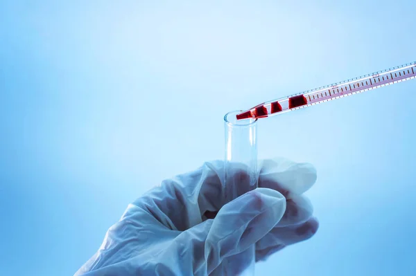 Medical laboratory. A hand in a medical glove pours blood from a pipette into an empty test tube on a blue background. Laboratory tests. Close-up.