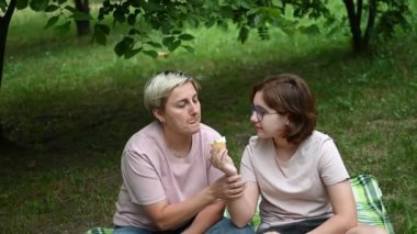 Mom and daughter eat ice cream sitting on a blanket in the park. Joint holidays with children.