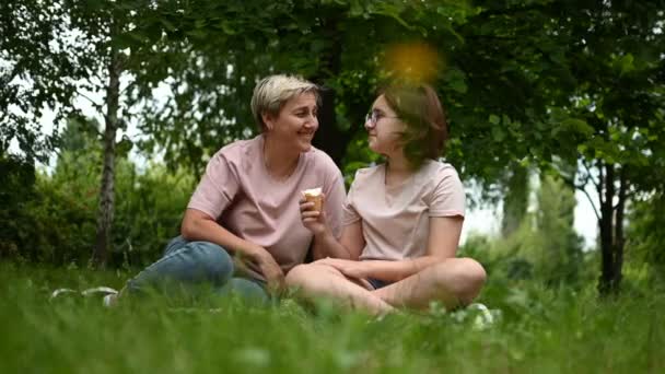 母と娘は公園の毛布の上に座ってアイスクリームを食べる 子供との合同休日 — ストック動画