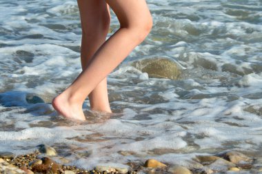 Kızın bacakları güneşin altında bir çakıl taşı plajında sörf yapıyor. Turizm kavramı.