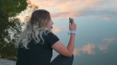 Şirin, güzel sarışın bir kız telefonuyla nehir manzarası çiziyor. Turizm ve seyahat kavramı