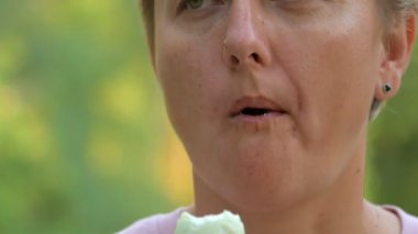 Kısa saçlı sarışın bir kız haşlanmış yumurtayı yeşil doğanın arka planında yer, hızlı ve ısrarla çiğner.