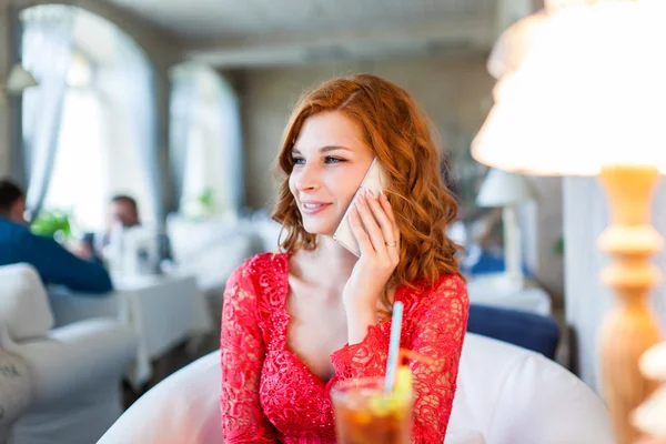 Frau in rotem Kleid sitzt mit ihrem Handy in einem Café — Stockfoto