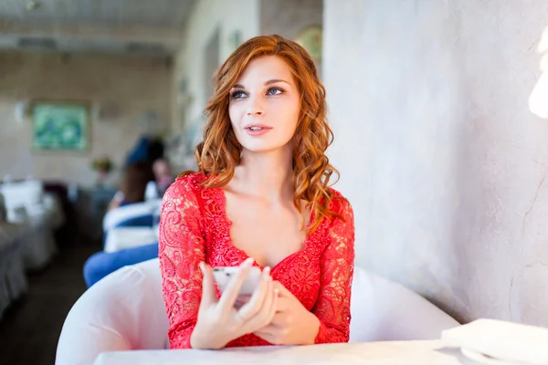 Frau in rotem Kleid sitzt mit ihrem Handy in einem Café — Stockfoto