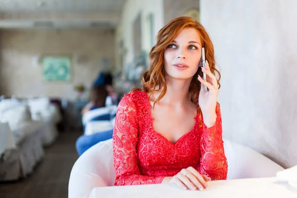 Женщина в красном платье сидит в кафе со своим мобильным телефоном — стоковое фото