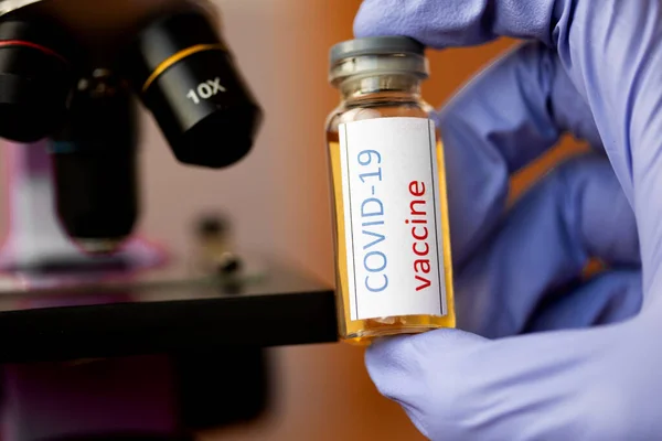 Врач или лаборант держит трубку с ковид-19 вакцины и микроскопа. — стоковое фото