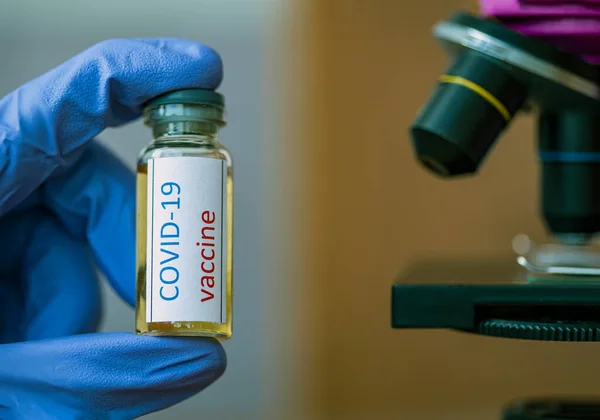 Врач или лаборант держит трубку с ковид-19 вакцины и микроскопа. — стоковое фото