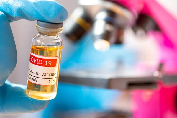 Врач или лаборант держит трубку с ковидовой вакциной рядом с микроскопом. — стоковое фото