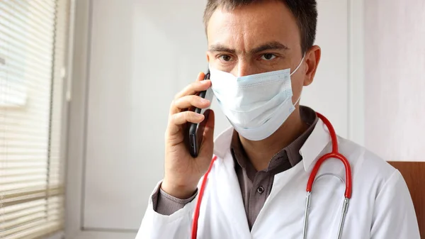 El médico preocupado con una máscara quirúrgica en la cara está hablando por teléfono —  Fotos de Stock