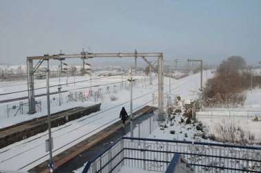 Karda tren istasyonu platformu ve yalnız yürüyen bir yolcu.