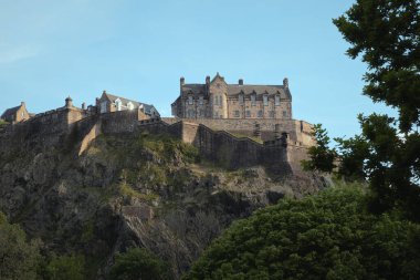 Edinburgh Kalesi, İskoçya 'daki Castle Rock' ta görkemli bir şekilde duruyor. Tarihi kale yemyeşil ile çevrili ve berrak bir gökyüzünün altında yumuşak akşam ışığı ile aydınlanıyor..