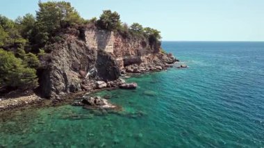 Türkiye 'nin Antalya kenti Phaselis Körfezi yakınlarındaki çam ormanıyla çevrili kayalık kıyı şeridi ve turkuaz sularının insansız hava aracı görüntüsü. Temiz Akdeniz ve dağ manzarası.