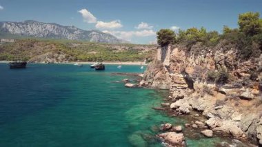 Türkiye 'nin Antalya Körfezi' nin mavi sularında yelkenli bir geminin havadan görünüşü. Açık gökyüzü, sakin deniz ve uzaktaki manzaralı kıyı dağları..