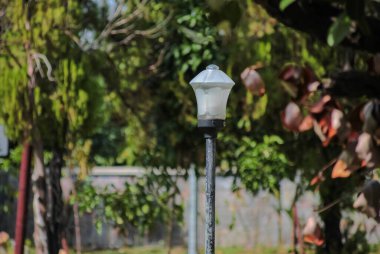 Bahçe lambası açık havada güneşli parkın yeşil ortamında duruyor..