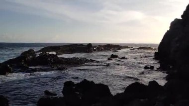 Okyanus dalgaları gün batımında kıyıdaki kara lav kayalarına çarpıyor..