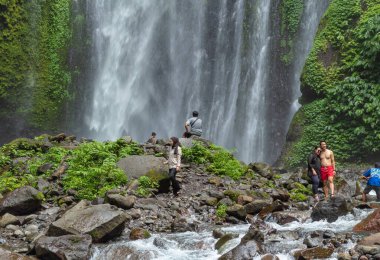LOMBOK UTARA, İNDONEZYA - 27 HAZİRAN 2025 - Tiu Kelep Şelalesi, Kuzey Lombok, Endonezya 'yı ziyaret eden turistler, kayalık arazide geziniyor ve akıntıya karşı kürek çekiyorlar.