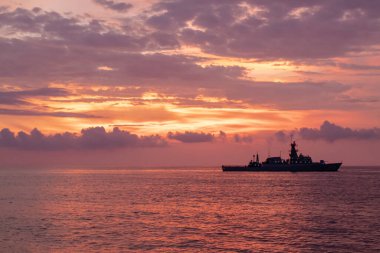 Dramatik günbatımına karşı savaş gemisi silueti.