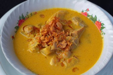 Endonezya 'nın zengin ve aromatik Lontong Sayur Kuning' inin (Hint cevizli pirinç keki) yakın planında, üzerinde kızarmış soğan, Lombok, Endonezya 'dan lezzetli ve doyurucu bir yemek var..