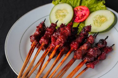 Lombok Adası 'ndan ünlü Endonezya spesiyali Sate Rembiga' nın yüksek açılı görüntüsü. Terbiye edilmiş ve ızgara baharatlı sığır eti parçaları bambu şişlerinin üzerinde, temiz beyaz bir seramik tabakta güzelce sunuluyor..