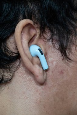 Kulağında mavi kablosuz kulaklık modern ses teknolojisini ve dijital yaşam tarzı ve kolaylığı için kişisel dinlemeyi gösteriyor