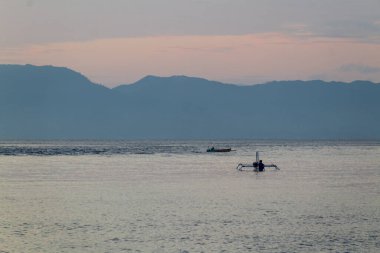 Huzurlu okyanusta sabah erken saatlerde dağ manzaralı küçük bir yelkenli, seyahat için fotokopi alanı ile geniş açılı yakalanır.