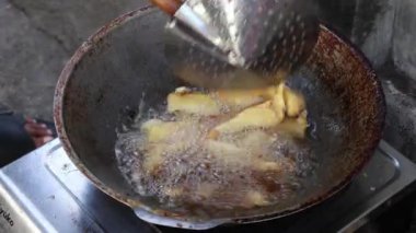 Doğal ışıkta yıkanmış eski bir tavada yiyecek kızartma, kaynayan yağ ve metin kaplaması için kopyalama alanı ile geleneksel bir aşçılık sahnesi tasvir ediliyor