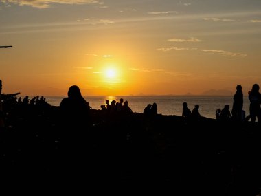 Siluetli insanlar gün batımında plajda toplanır, altın ışıkla yıkanırlar, seyahat ve eğlence için rahatlatıcı bir atmosfer yaratırlar.