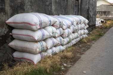 Yığınlanmış çuvallar, kırsal alandaki tarımsal depolama ve dağıtım ağını temsil eden fotokopi alanıyla eski duvara yaslanıyor.