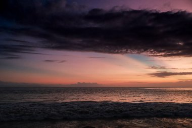 Canlı renkler ve doğal ışık ile dramatik günbatımı gökyüzü altında okyanus dalgaları, ilham verici ve seyahat içeriği için ideal bir deniz manzarası.