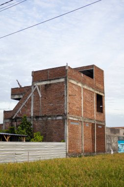 Yeşil alan ve temiz gökyüzü tarafından çerçevelenmiş, inşaat halindeki tamamlanmamış tuğla bina, emlak yatırımları kavramları için kopya alanı sağlıyor