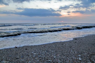 Huzurlu deniz manzarası kayalık kıyı şeridi ve pastel renkli bulutlar tatil ve manzara görüntülerini çağrıştırıyor.